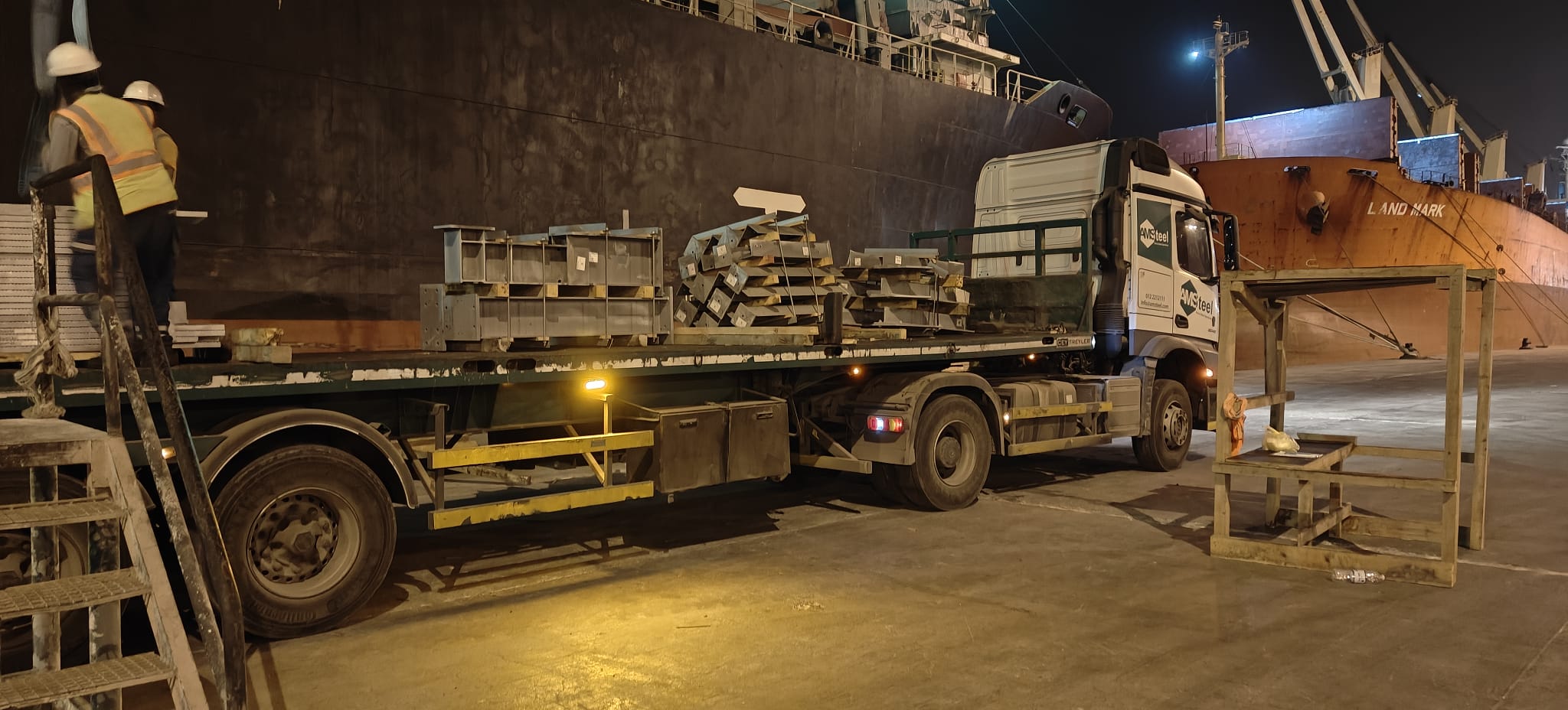 Harbour truck delivering steel structures to the ship side at night during round the clock loading